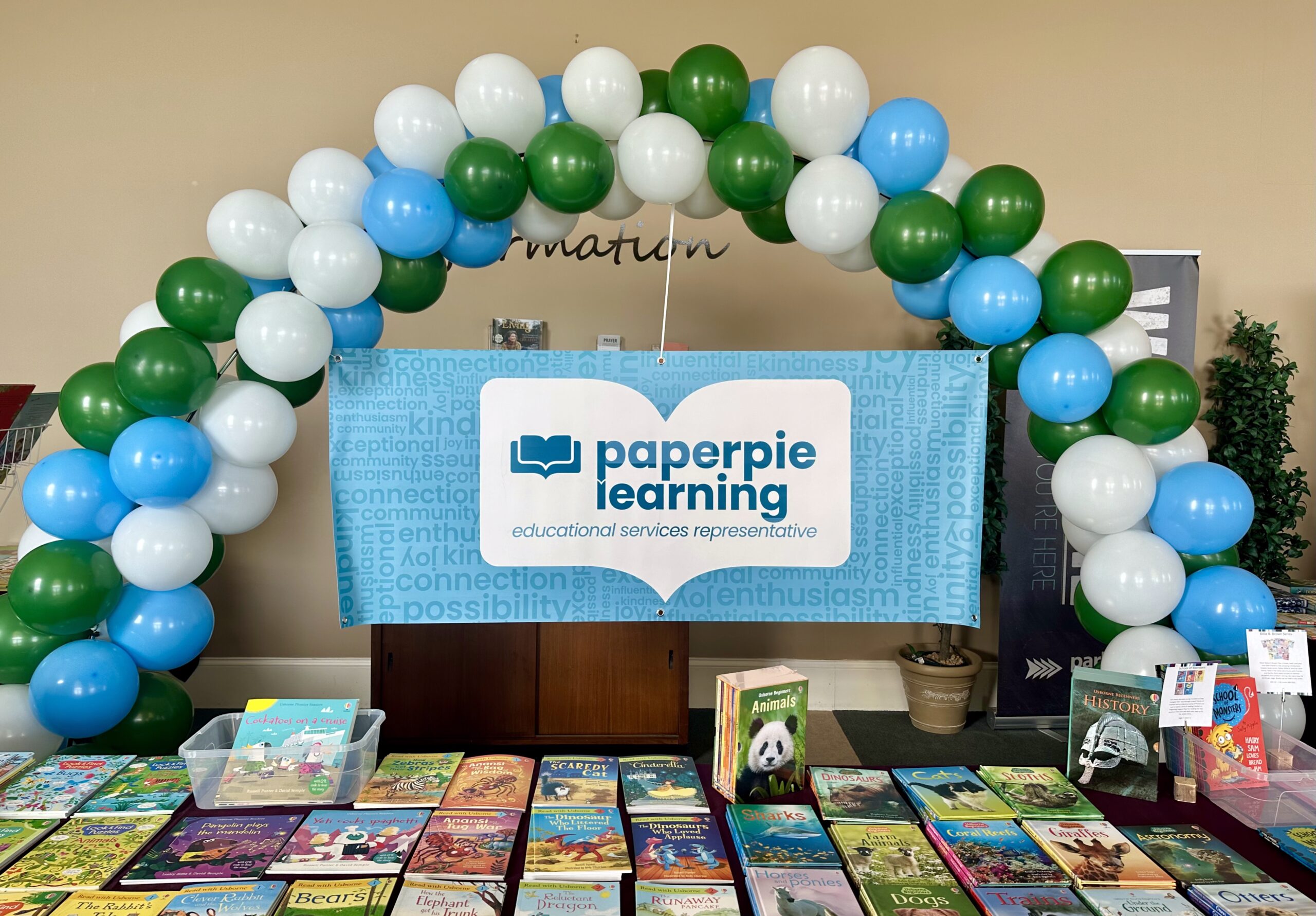 A Books With Jen book fair setup with tables full of PaperPie books and a balloon arch