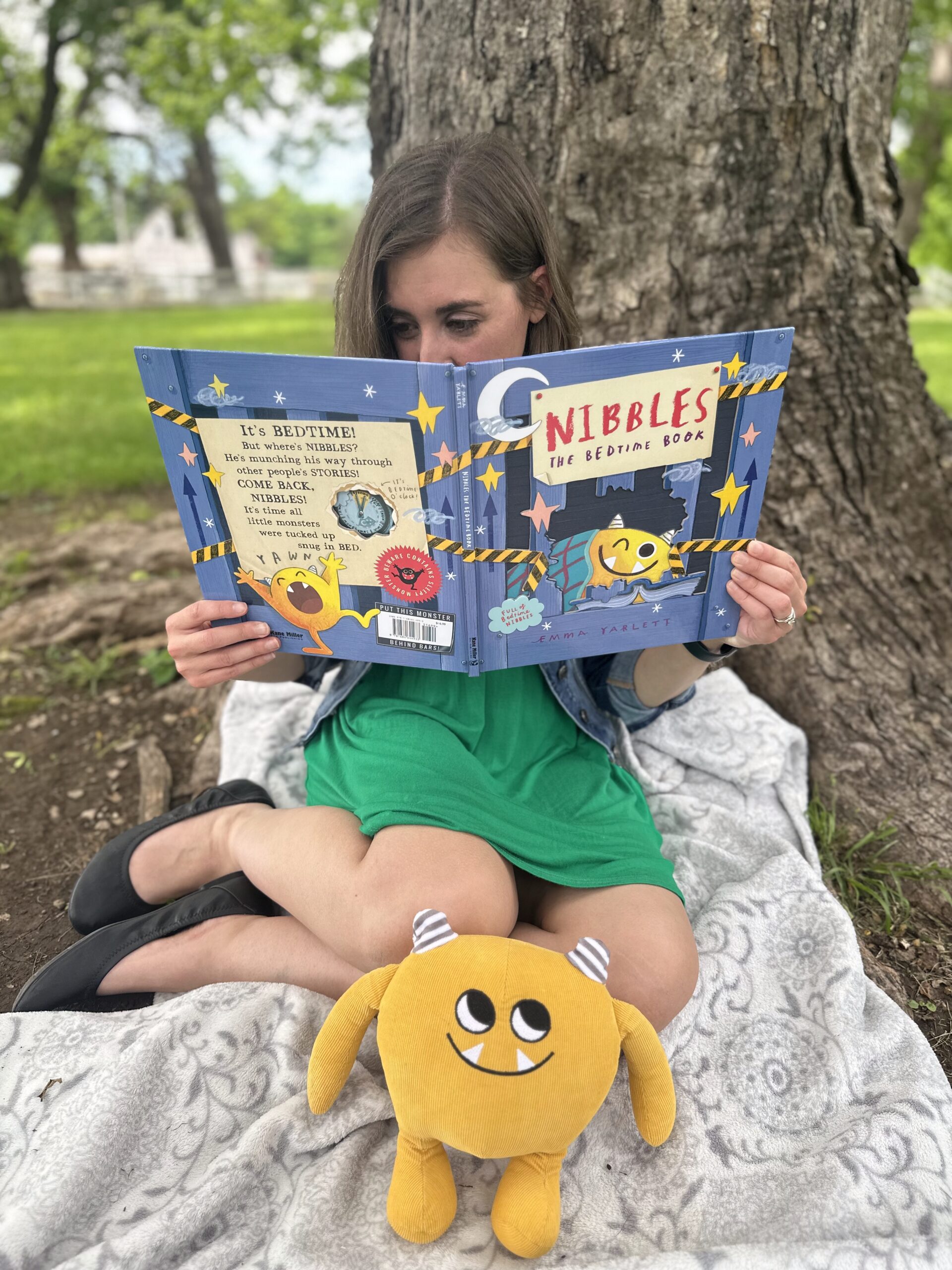Jen Williams reading a children's book outdoors under a tree